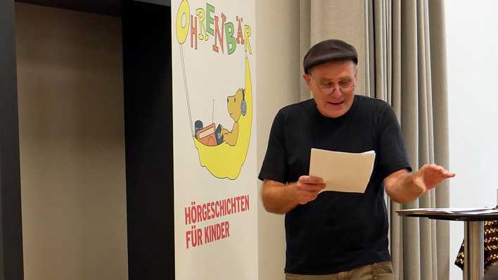 Autor Martin Klein liest, stehend mit einem Manuskriptblatt in der Hand (Quelle: rbb/OHRENBÄR/Jakob Senger)